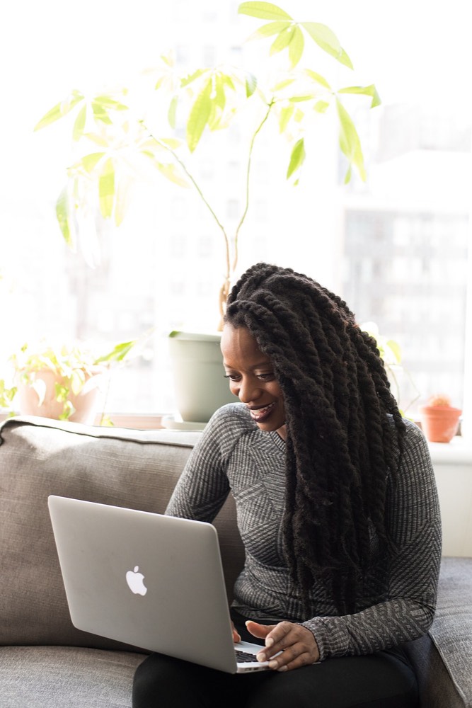 Woman smiling at her laptop on a sofa